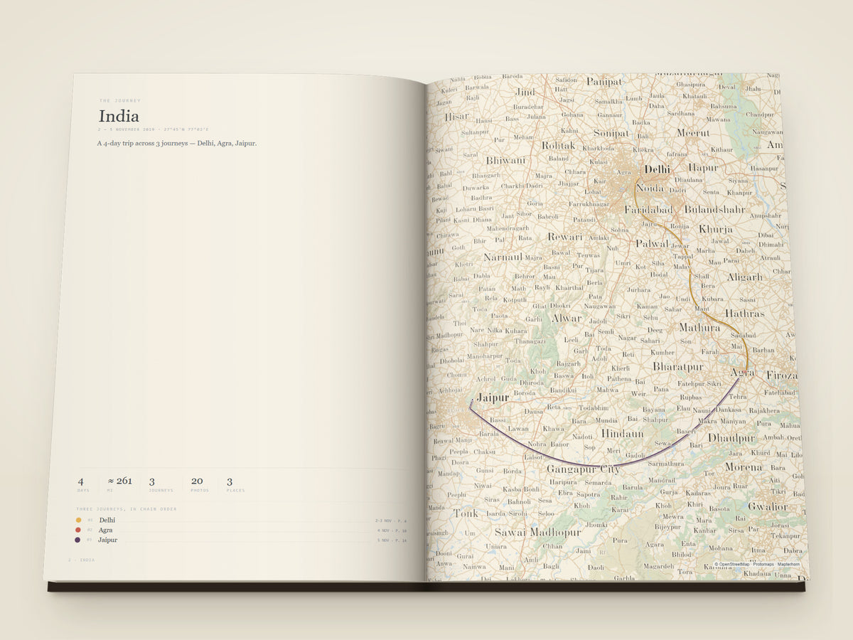 The same A4 portrait softcover Travel Book, open on the table. The opening spread of the book: four days in northern India — Delhi, Agra and Jaipur, drawn as one continuous route across a map of both pages, with the days, the distance, the number of photographs and every stop listed beside it