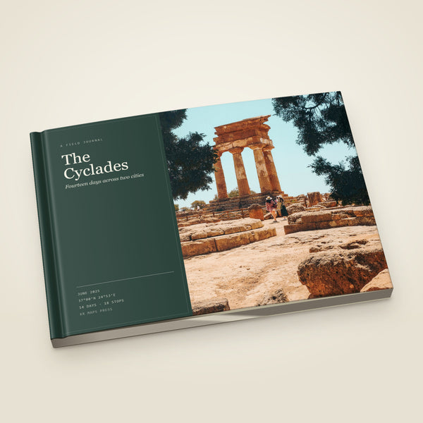kr-paper:kr-maps-travel-book-a5-softcover:hero:3831e735 — A A5 landscape softcover KR Maps Travel Book, closed on a table — a book of the Cyclades, the title set over one of the trip's own photographs