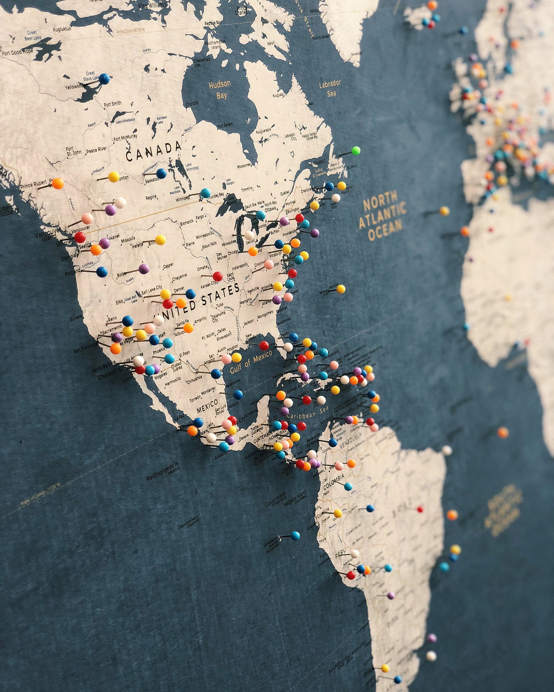 Close-up of a Blue and Gold Push Pin World Map by KR Maps with pins sticking out to mark travel destinations