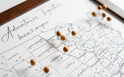 High-resolution close-up of framed 11x14" USA push pin map with wooden pins, featuring black-and-white design with labeled U.S. states and interstate highways. Desk-sized personalized map for tracking travels and adventures.