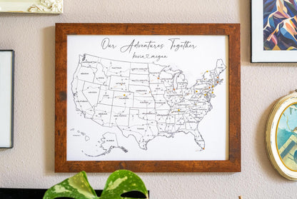 Framed 11x14" push pin USA map in black and white hanging on a wall, displaying labeled U.S. states and interstate highways with a minimalist design. Personalized travel map for tracking adventures.