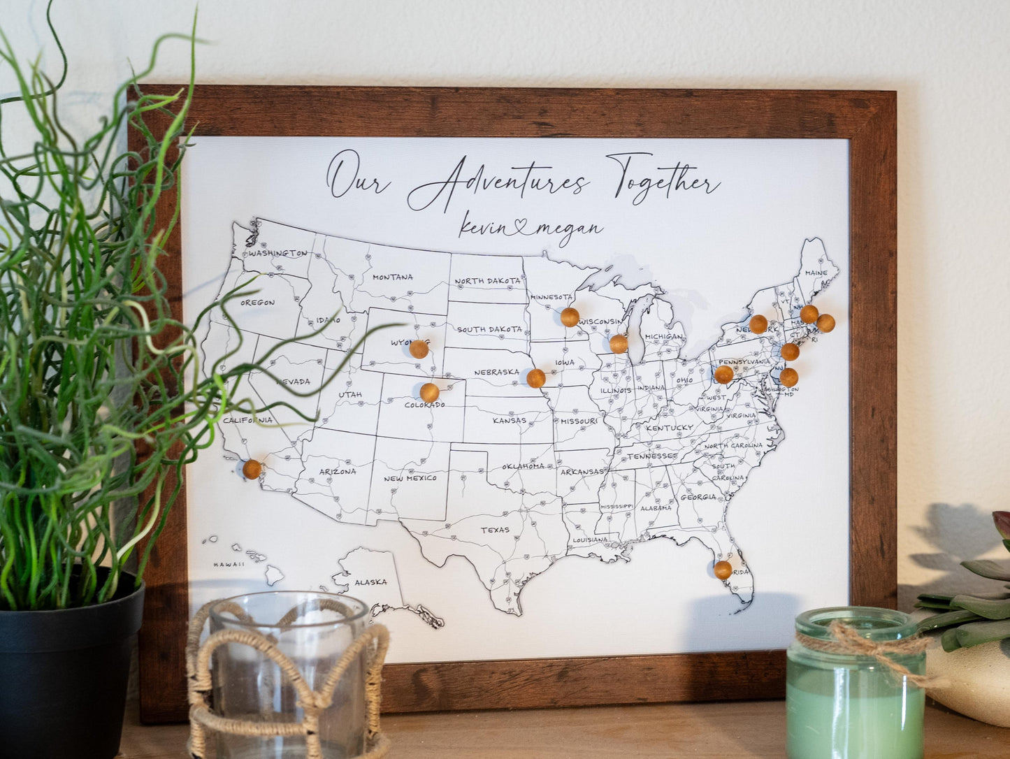 Framed 11x14" USA push pin map displayed on a mantle with candles and plants, featuring a black-and-white design with labeled states and highways. Decorative and personalized map for tracking travels