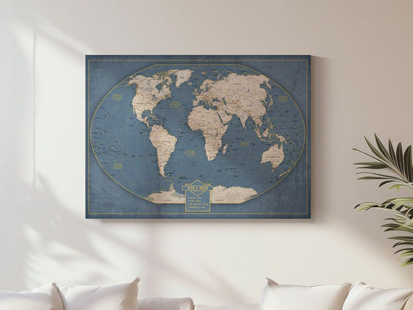 May include: A blue world map with a vintage look. The map is surrounded by a gold border and has a gold title that reads 'The World.' The map is displayed on a white wall with a plant in the background.