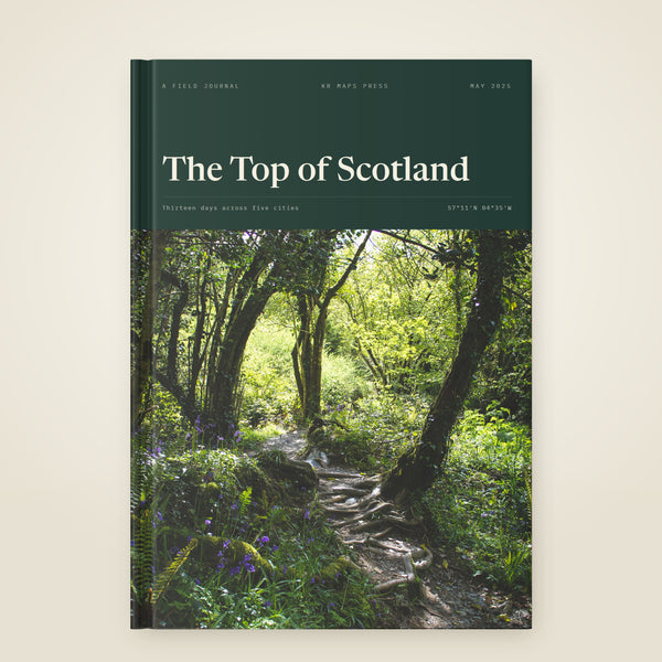 kr-paper:kr-maps-travel-book-a4-portrait-hardcover:hero:e2a94df1 — A A4 portrait hardcover KR Maps Travel Book, closed on a table — a book of the north coast of Scotland, the title set over one of the trip's own photographs