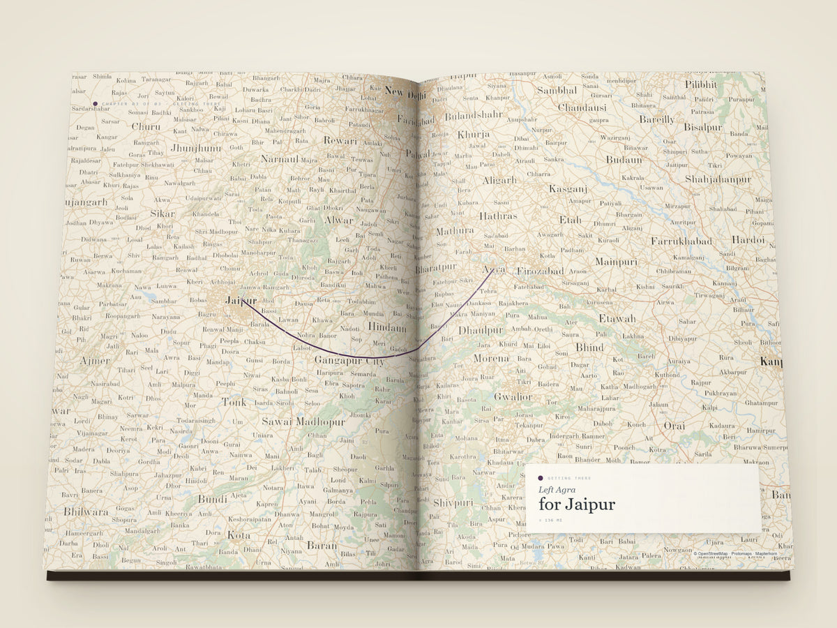 The same A4 portrait softcover Travel Book, open on the table. A getting-there spread — the leg from Agra to Jaipur drawn as a single arc across a map filling both printed pages, with a card noting the departure