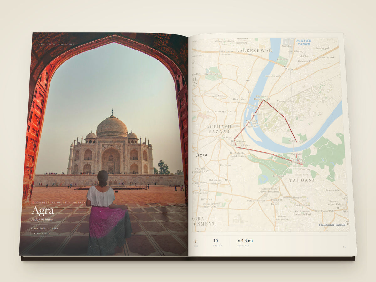 The same A4 portrait softcover Travel Book, open on the table. A chapter opening across both pages — the Taj Mahal seen through a red sandstone archway, filling the left page under the place name, facing a street map of Agra with the day's walk drawn across it: from the Taj west along the river to the Fort, over the bridge and down the far bank to Mehtab Bagh, with the chapter's days, photographs and distance set beneath
