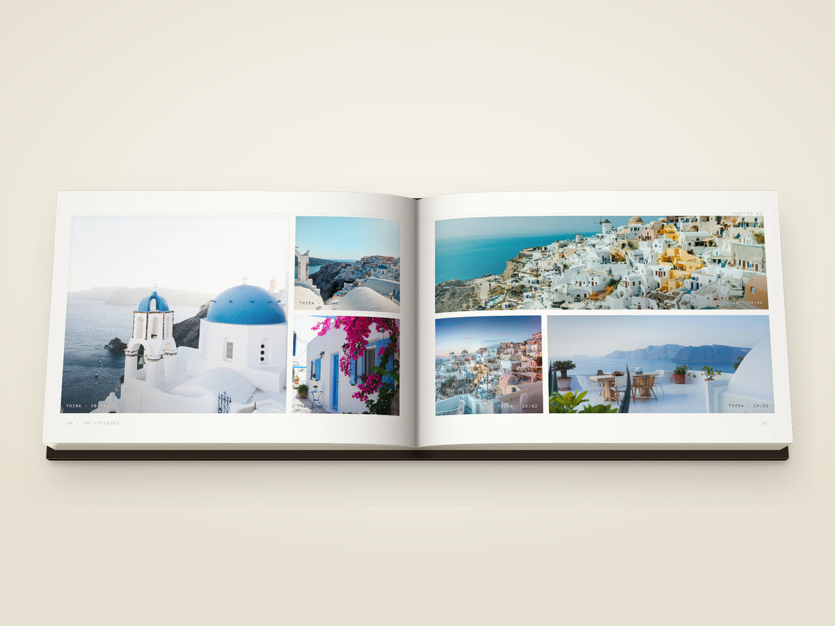 The same A5 landscape softcover Travel Book, open on the table. Two printed pages — six photographs from Santorini — blue domes over the sea, the white town on its cliff, bougainvillea over a blue door, the town spread wide along the caldera, the cliff at dusk and a terrace over the water
