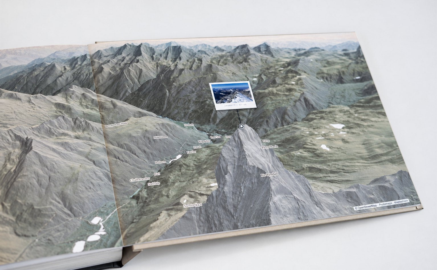 A printed summit spread, photographed: the Matterhorn in 3D relief across both pages, a photograph planted at its coordinates